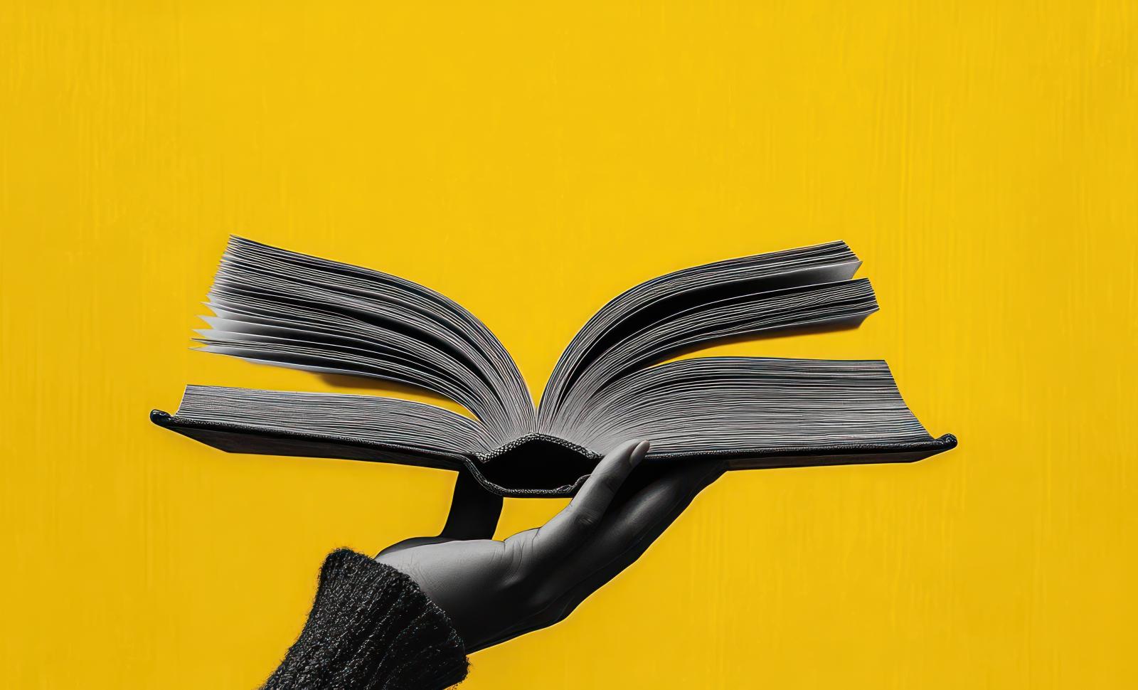 Hand holding book in front of yellow background