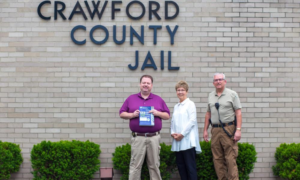 Fred Chinn, Rena Gower, Bill Rutan stand in front of Crawford County Jail holding donated book