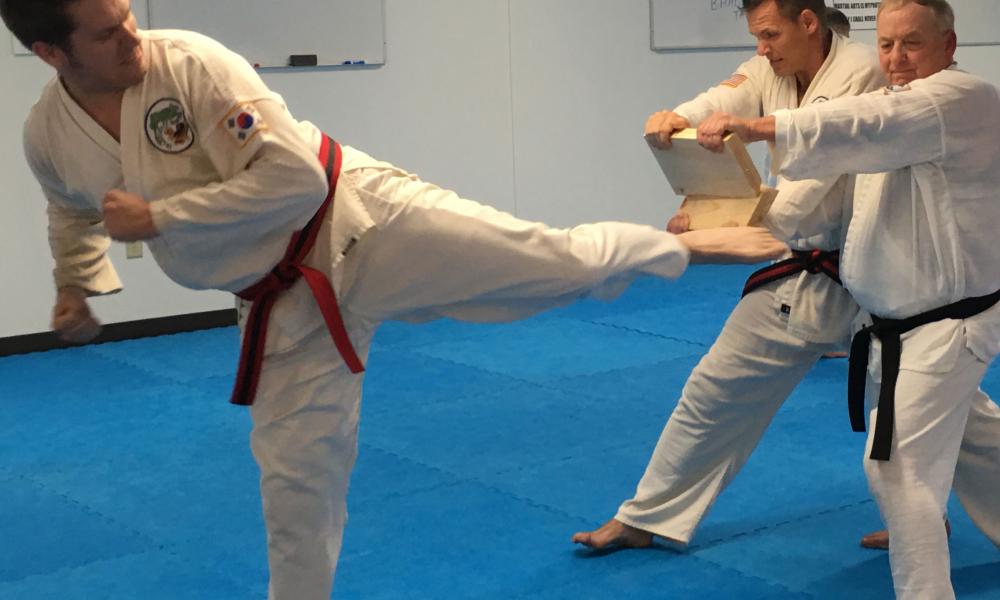 Man kicking a board in a martial arts class